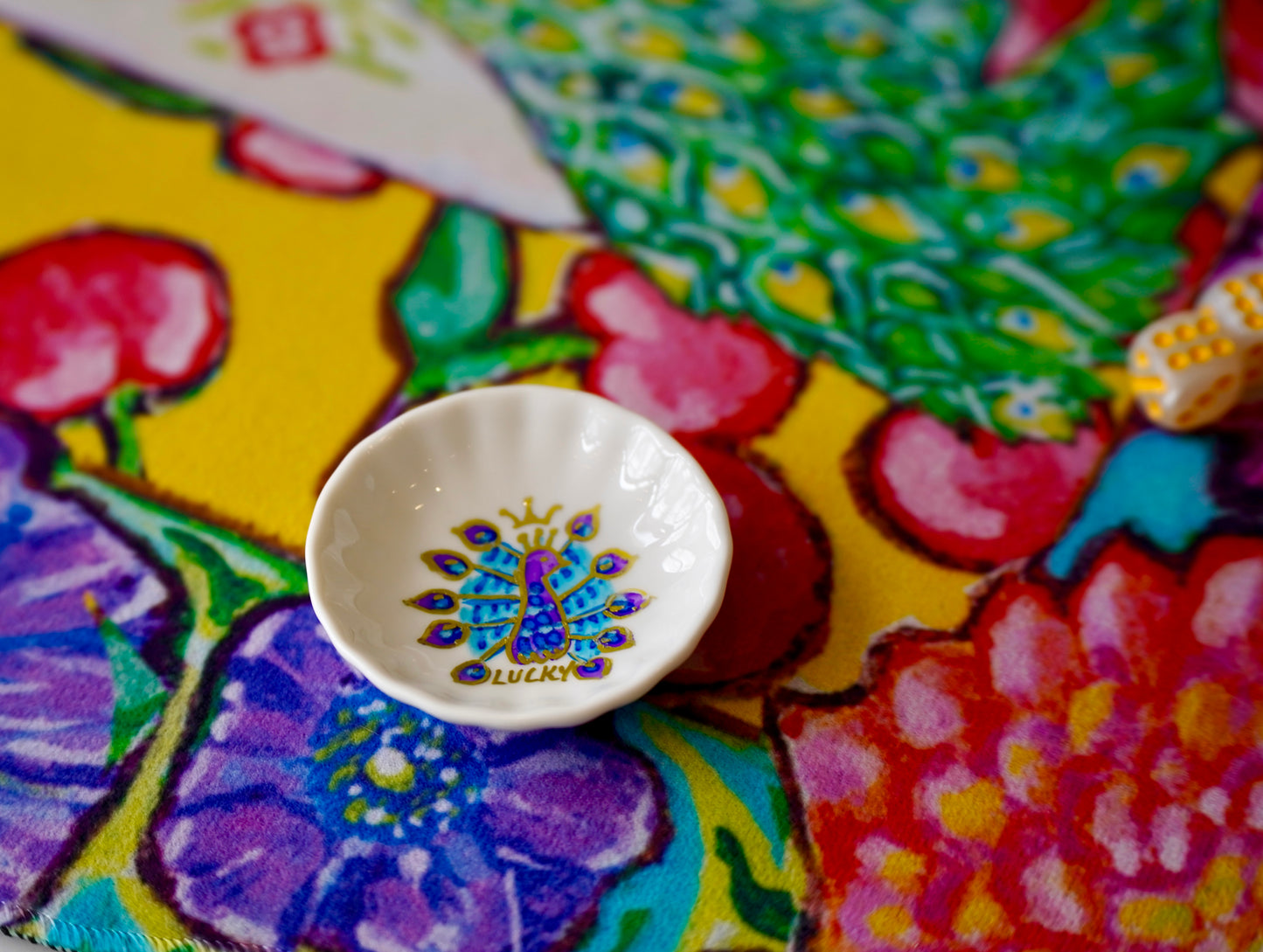 A handprinted dice dish to match a colorful mahjong mat featuring an original painting of peacocks, cherries, dahlias and anemones flowers.