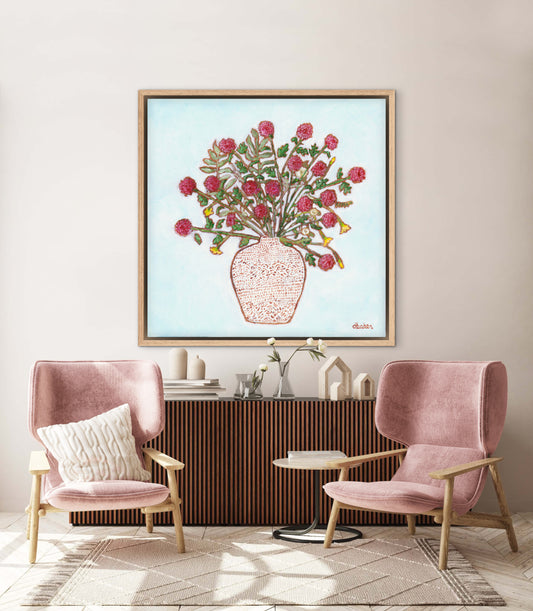 Framed artwork of a red dahlia floral arrangement on a light blue background, with a white patterned vase and plants on a wooden surface.
