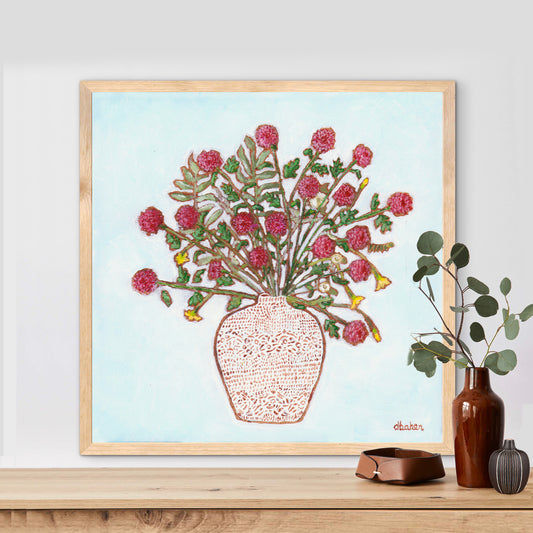 Framed artwork of a red dahlia floral arrangement on a light blue background, with a white patterned vase and plants on a wooden surface.