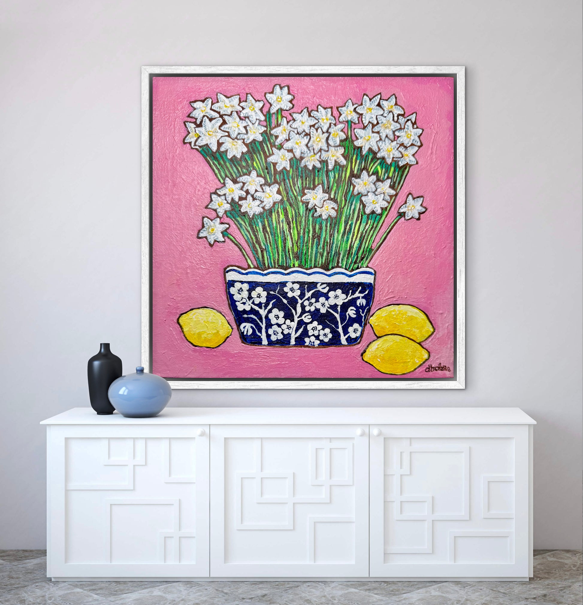 A whimsical painting of paperwhites in a blue and white floral vase surrounded by lemons against a bright pink background.
