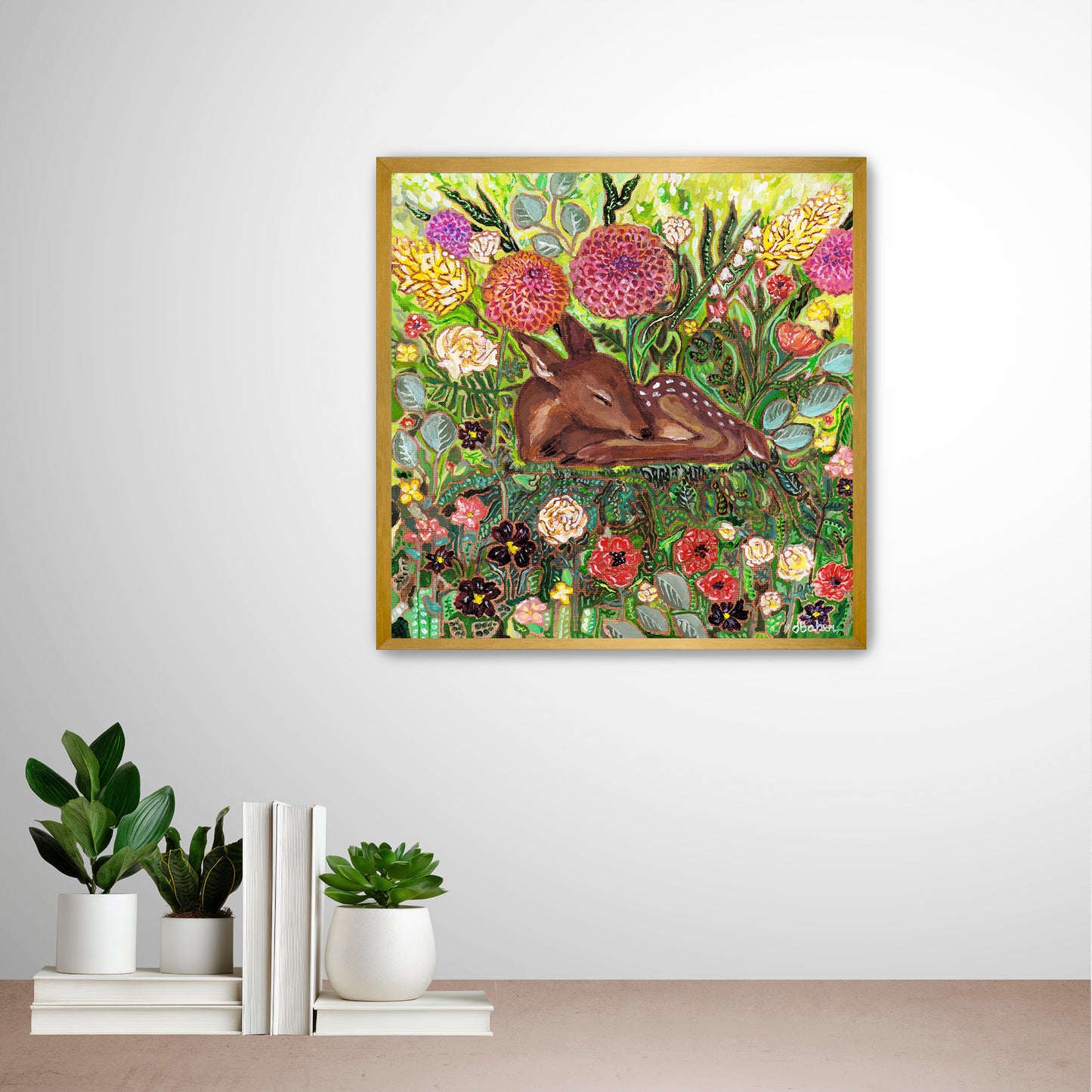 Framed artwork of a deer among flowers from Michigan Artist Deb Baker on a wall with decorative books and plants below. 