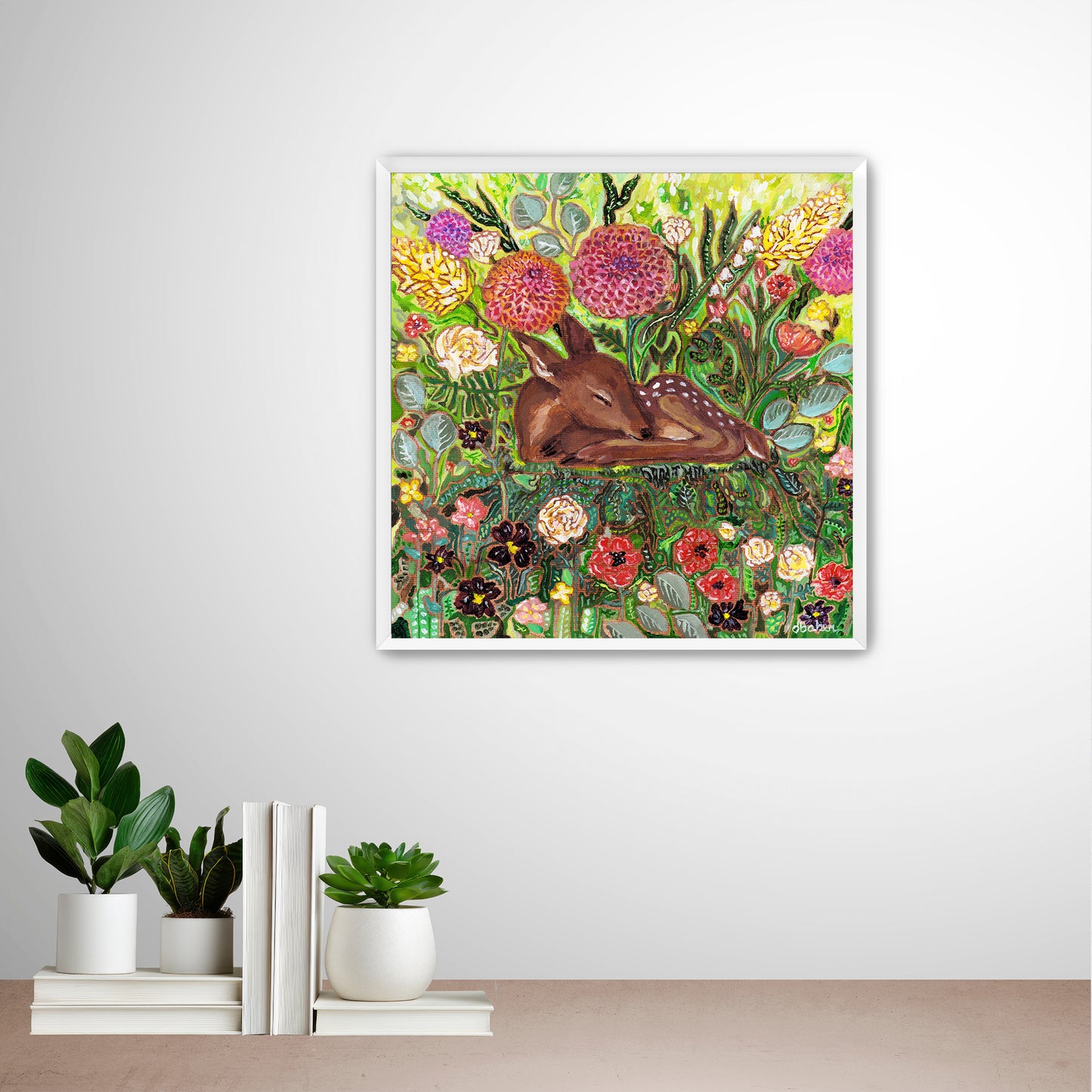 Framed artwork of a deer among flowers from Michigan Artist Deb Baker on a wall with decorative books and plants below. 