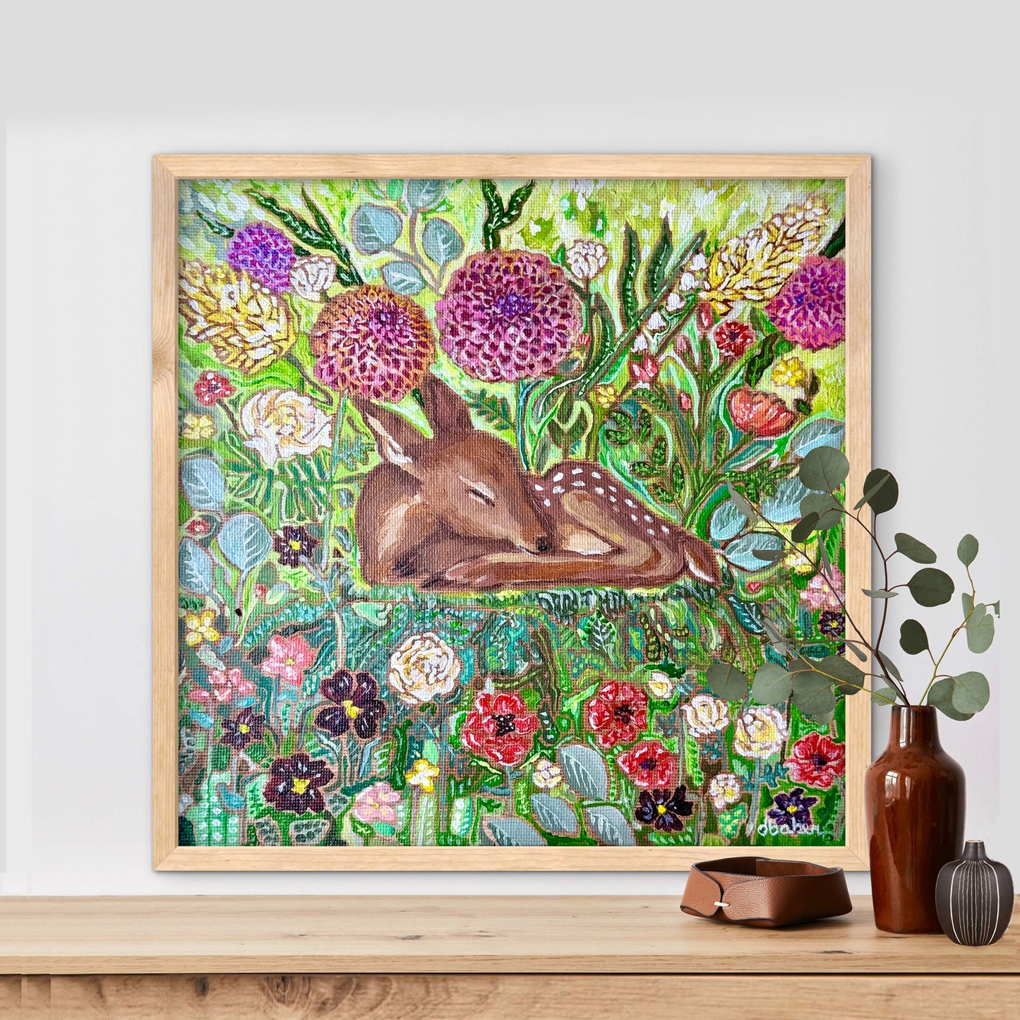 Framed artwork of a deer among flowers on a wall above a wooden shelf from Michigan Artist Deb Baker